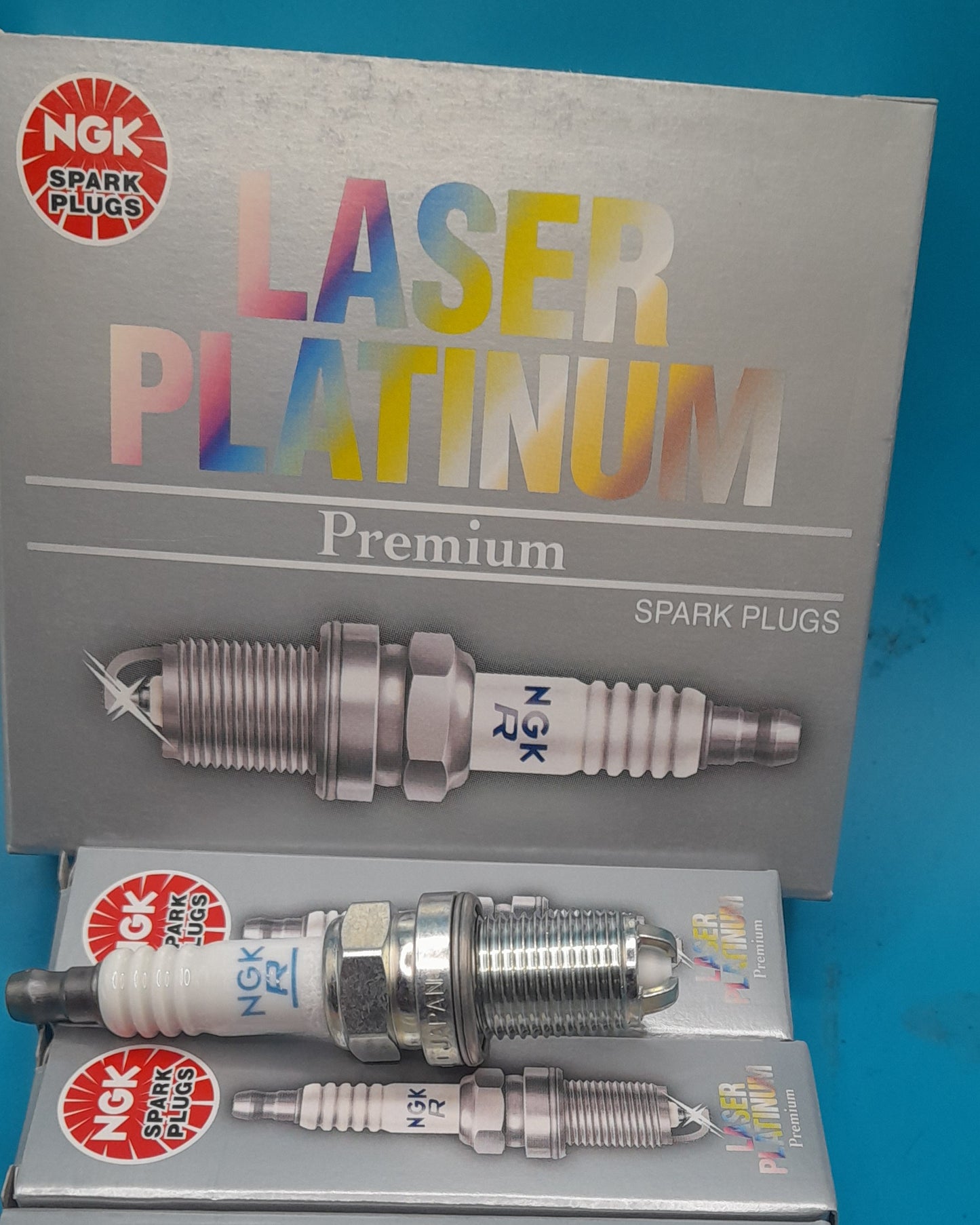 NGK Laser Platinum Premium spark plugs shown with their gray retail packaging box and two individual spark plugs on a bright blue background.