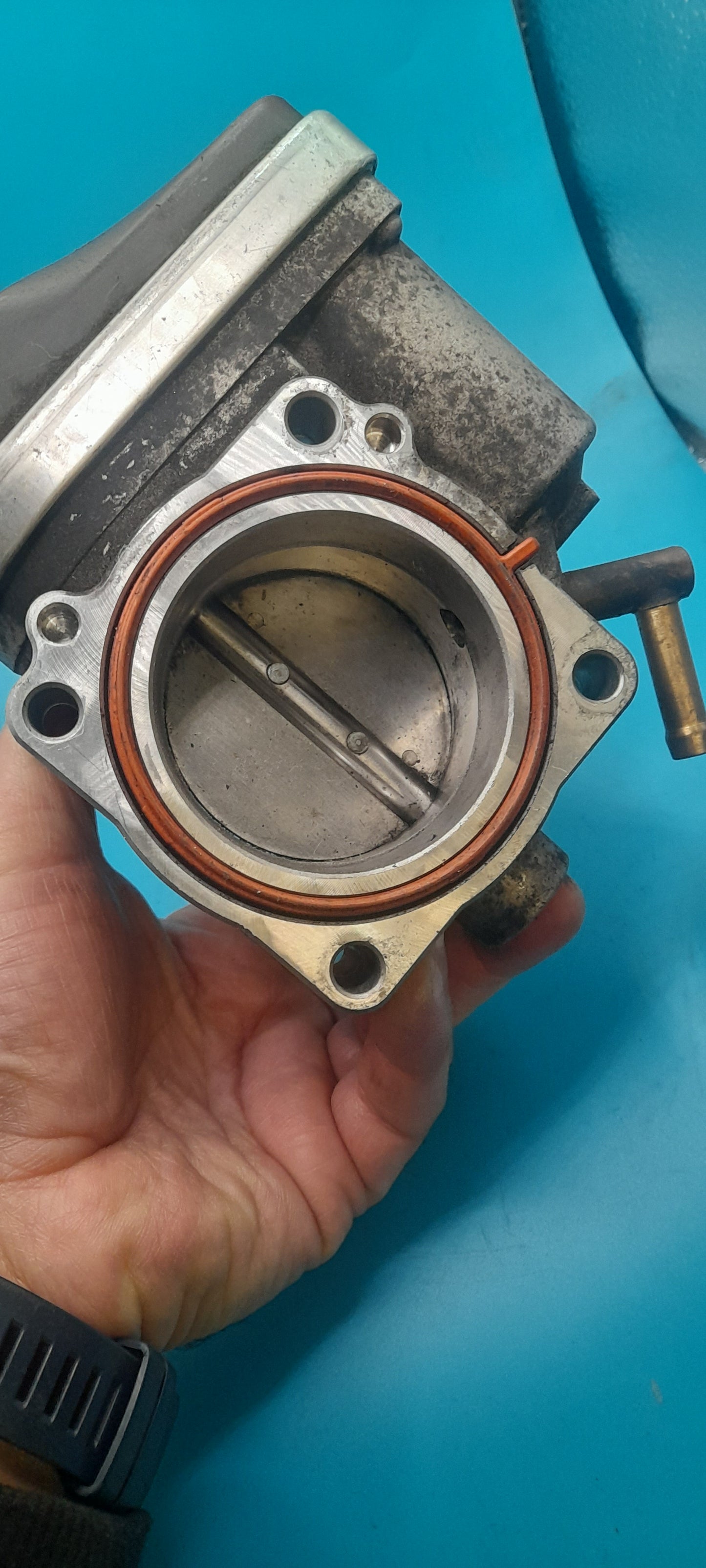 Hand holding a mechanical throttle body against a blue background