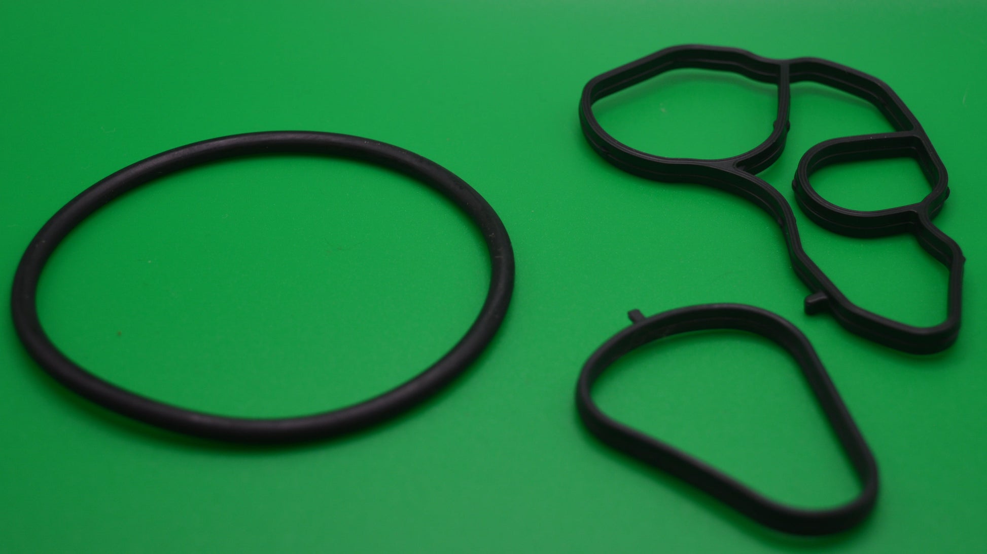 A set of black rubber gaskets and oil drain plugs on a green background.