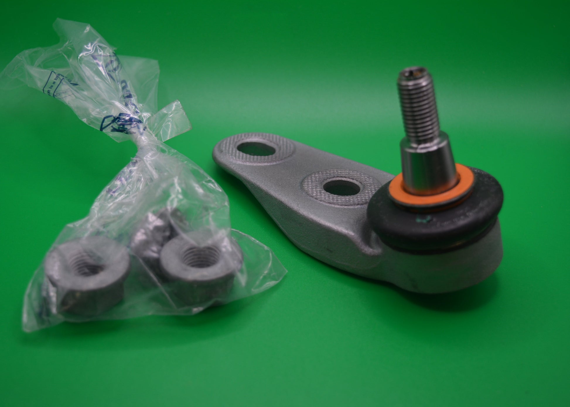 A silver-colored outer ball joint for a vehicle, displayed alongside its packaging on a green background.