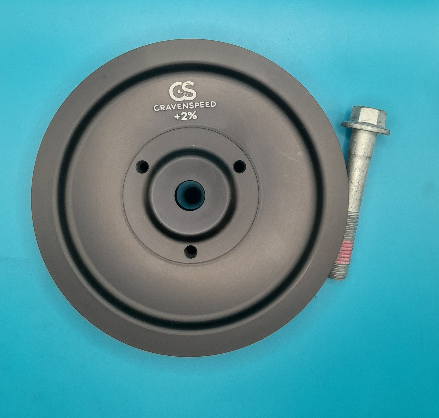 A black anodized aluminum lightweight crank pulley with the logo 'CravenSpeed' and text '+2%' on it, alongside a metal crank bolt, for mini cooper s