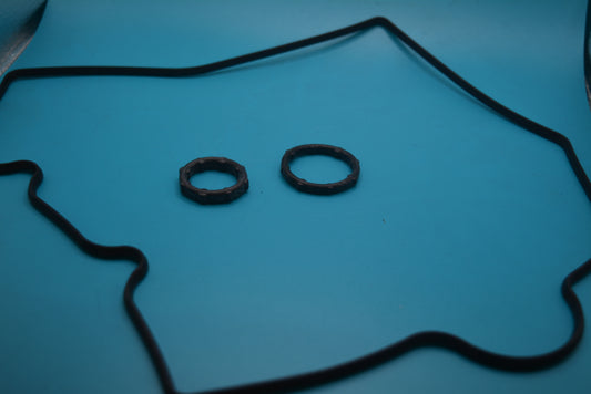 A set of black front timing cover gaskets on a blue background, including a timing cover seal and oil pump orings.