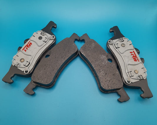 A set of four rear TRW brake pads for a Mini Cooper, displayed on a blue background.
