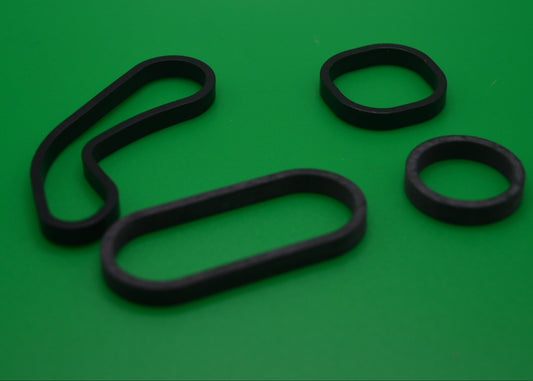 A set of black gaskets of different shapes laid out on a green background.