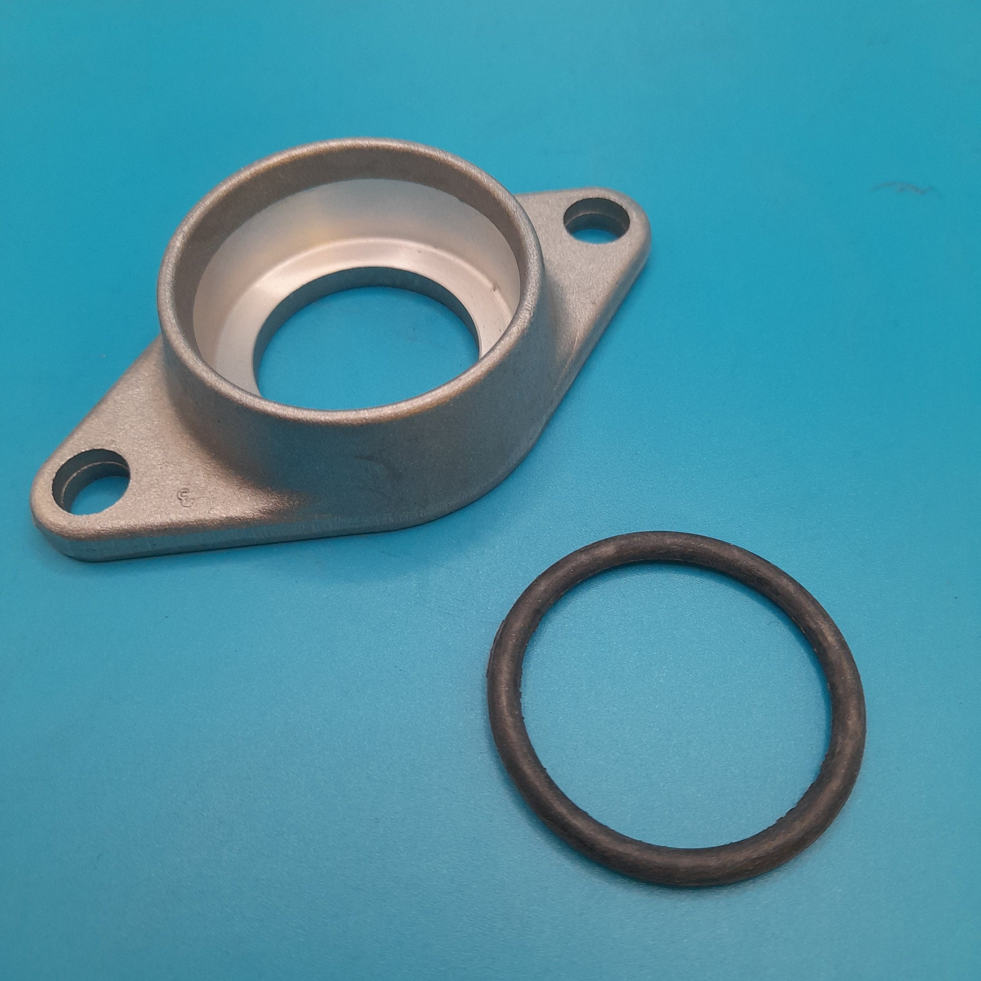 A metal water pump to engine block flange plate with a central hole and two mounting holes on a blue background.