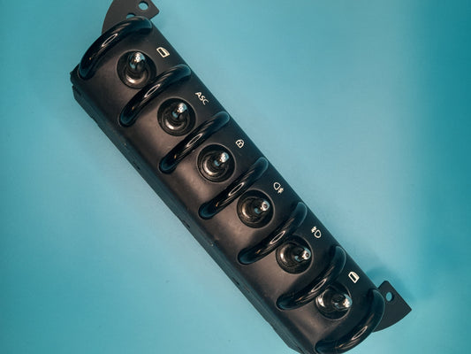A black Mini Cooper door window switch with multiple control knobs, displayed against a blue background.
